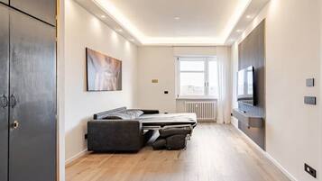 Ein modernes Hotelzimmer mit Bett, Flachbildfernseher und einem fensterbelaubten Fenster.