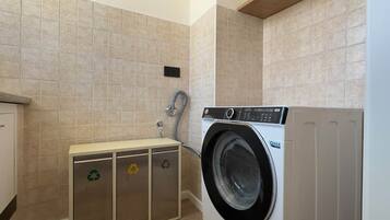 A laundry room with a washing machine, a cabinet with recycling symbols, and a tiled wall.