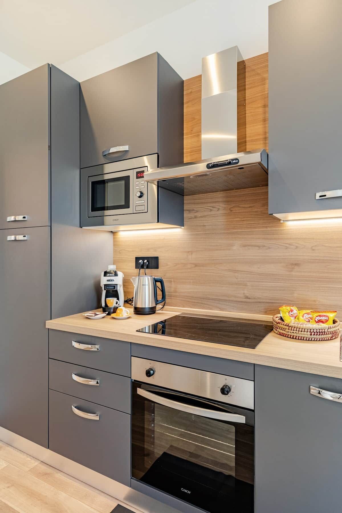 Een moderne keuken met grijze kastjes, een ingebouwde magnetron, een koffiezetapparaat en een waterkoker op het aanrecht.