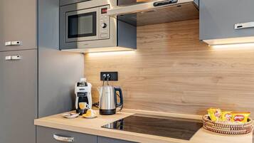 A modern kitchen with grey cabinets, a built-in microwave, a coffee maker, and a kettle on the countertop.