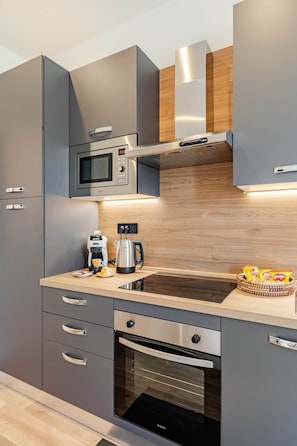 A modern kitchen with grey cabinets, a built-in microwave, a coffee maker, and a kettle on the countertop. - Charme Vittoria | Elegant Apartment in Downtown Asti (Asti)