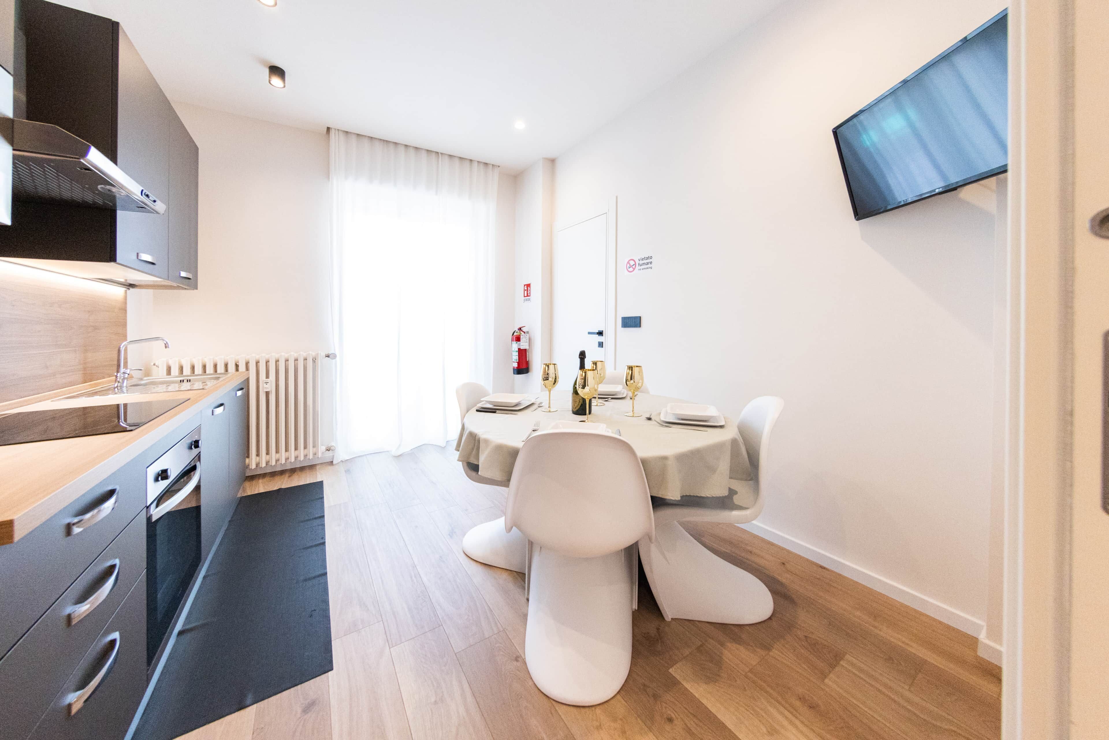 Een moderne keuken met een ingebouwde kookplaat, een eethoek met een tafel voor twee personen, en een flatscreen televisie aan de wand.