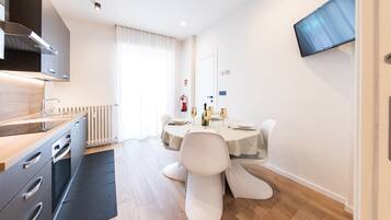 Een moderne keuken met een ingebouwde kookplaat, een eethoek met een tafel voor twee personen, en een flatscreen televisie aan de wand.