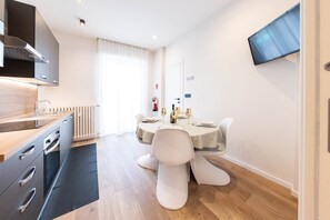 A modern kitchen with a built-in stove, a dining area with a table set for two, and a flat-screen TV mounted on the wall. - Charme Vittoria | Elegant Apartment in Downtown Asti (Asti)