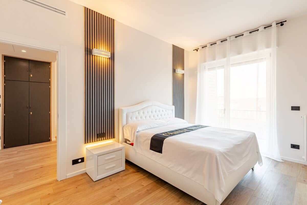 Ein modernes Schlafzimmer mit einem Bett, Nachttischen, einem Kleiderschrank und einem Fenster mit Vorhängen.