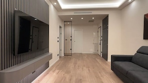 A modern living room with a flat-screen TV mounted on a wall, a sofa, and a wooden floor.