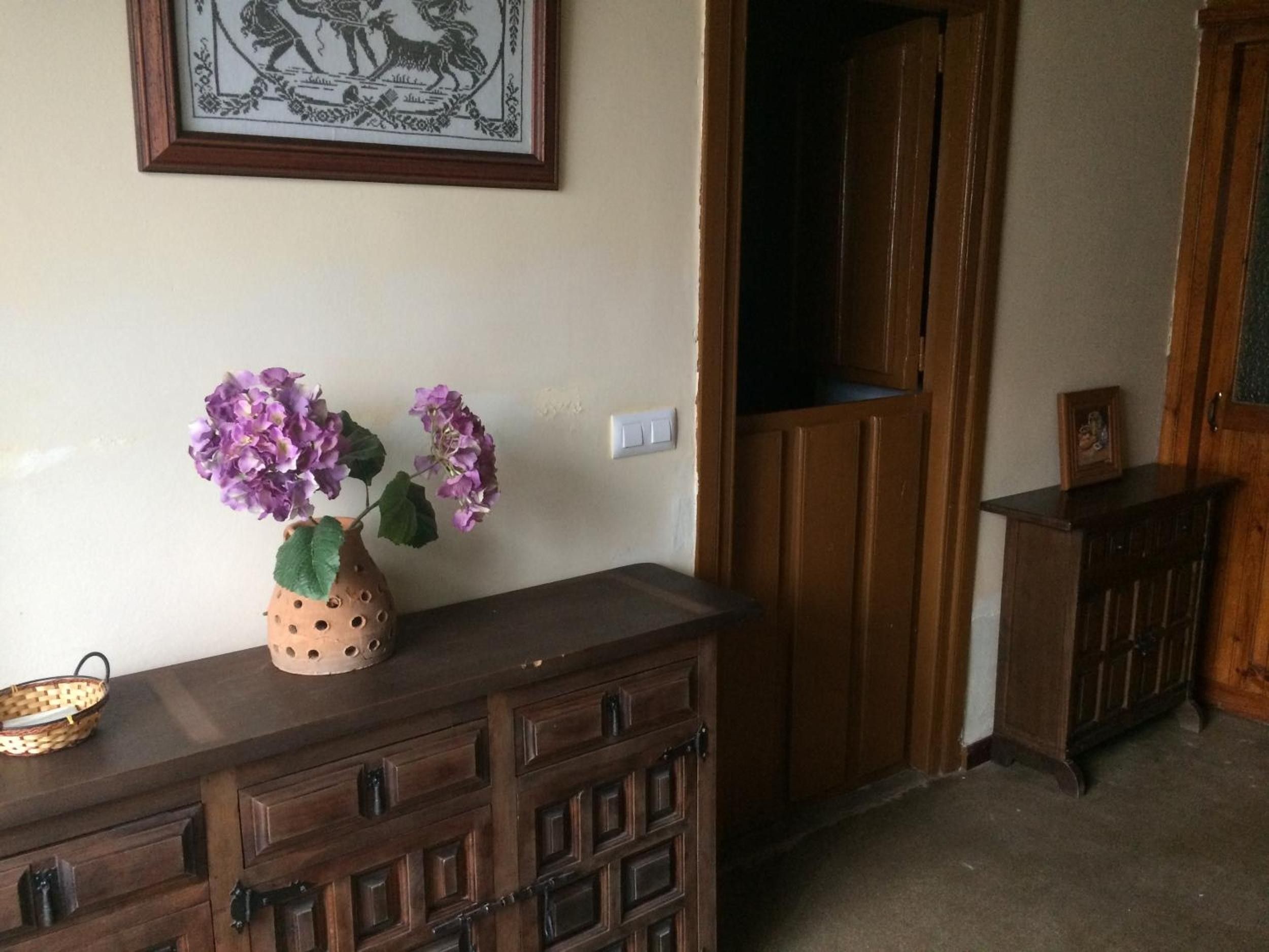 A wooden dresser with drawers and a vase of purple flowers.