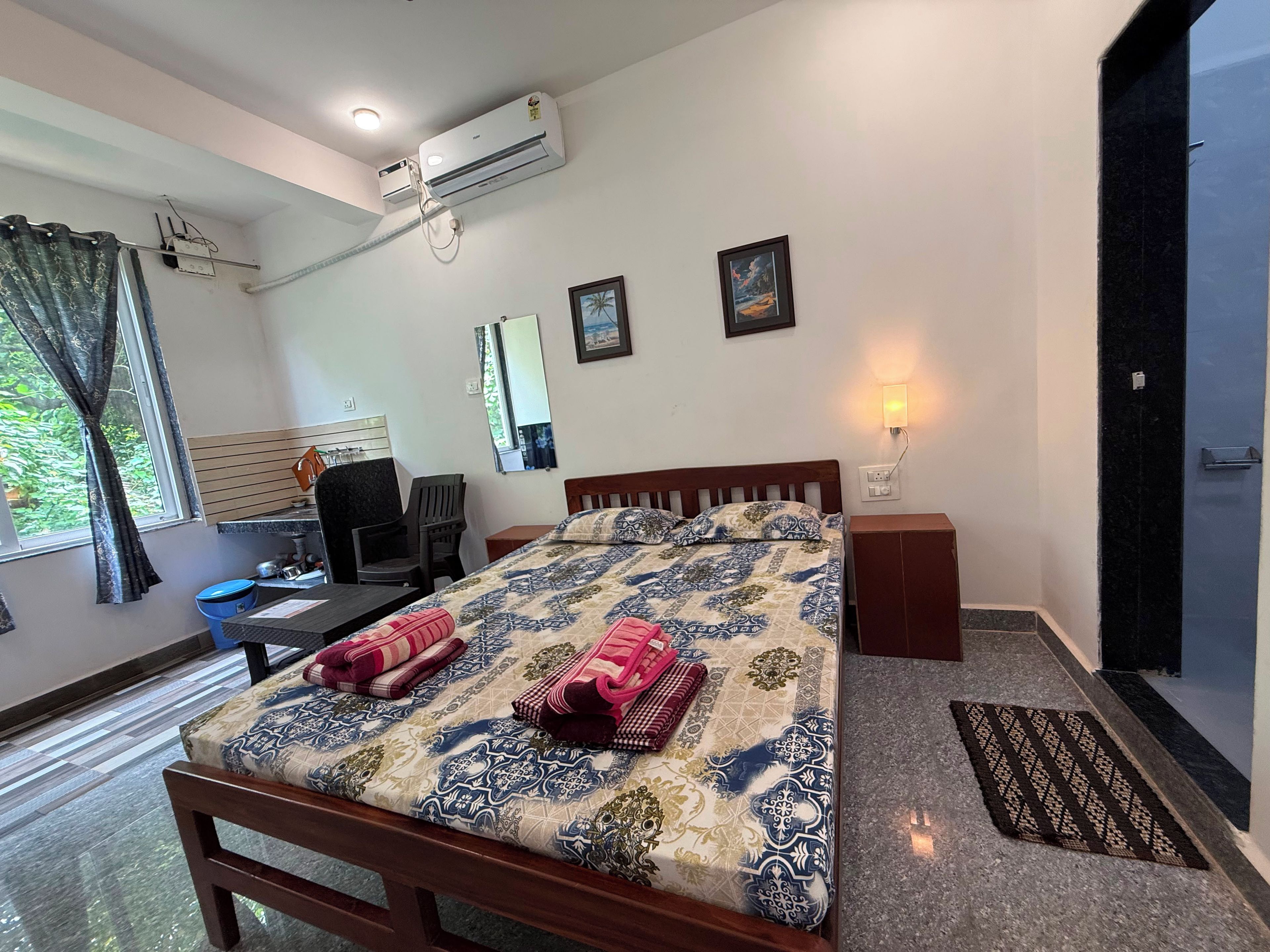 Habitación de hotel con cama, mesita de noche, escritorio, silla, aire acondicionado y puerta.