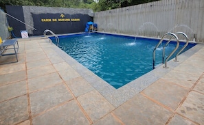 A rectangular swimming pool with a tiled deck, metal pool ladders, and a sign with text. - Studio Arambol Escape R8 Couple Friendlly (Arambol)