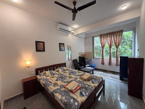 A hotel room with a bed, desk, chair, air conditioning unit, and a window with curtains. - Studio Arambol Escape R8 Couple Friendlly (Arambol)