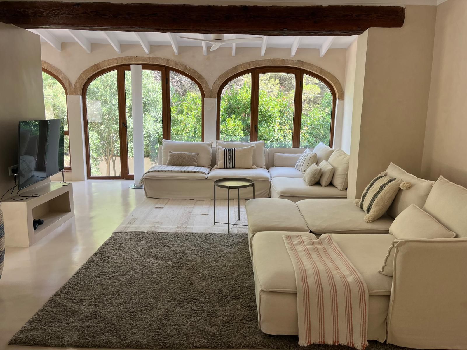 A modern living room with a large sectional sofa, a flat-screen TV, and a view through arched windows.