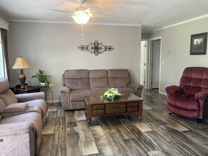 A living room with a brown sofa, a red recliner, a wooden coffee table with a floral centerpiece, and a ceiling fan. - Country life,come and relax! (Crossville)