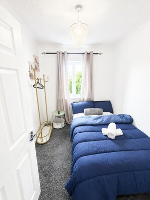 A bedroom with a bed, a hanging light fixture, a window with curtains, a coat rack, and a small round table. - Elegant 2 Bedroom Apartment in Erith Breathtaking River Thames View (Erith)