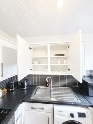A modern kitchen with a built-in dishwasher, a sink with a faucet, and a countertop with a kettle and toaster. - Elegant 2 Bedroom Apartment in Erith Breathtaking River Thames View (Erith)