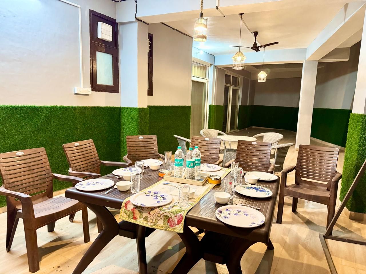 Uma sala de jantar com uma mesa posta para seis pessoas, rodeada por cadeiras, com um ventilador de teto e luminárias pendentes.