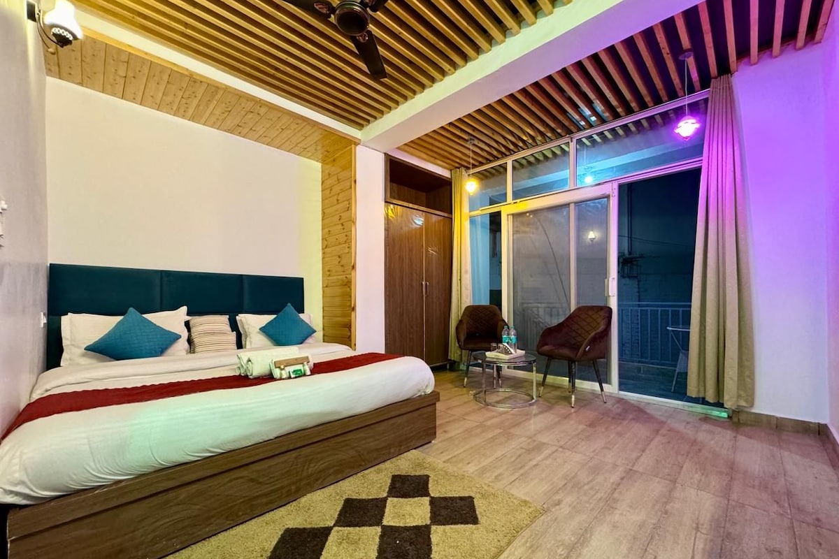 A bedroom with a bed, a chair, a small table, and a view of the outside.
