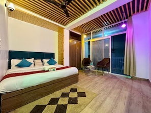 A bedroom with a bed, a chair, a small table, and a view of the outside. - Mid Hills (Kasauli)