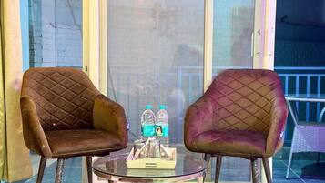 Two armchairs with a quilted pattern, a glass table with a tray of bottled water, and a wicker chair in the background.