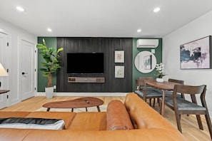 A modern living room with a flat-screen TV, a dining table with chairs, a sofa, and a potted plant. - Modern 4BR Container Home | Epic Private Rooftop (Pittsburgh)