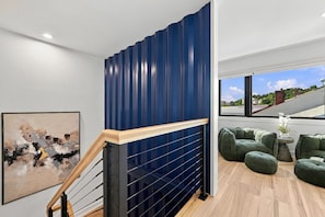 A modern interior with a wooden staircase, a blue accent wall, a contemporary art piece, and a seating area with green upholstered chairs. - Modern 4BR Container Home | Epic Private Rooftop (Pittsburgh)