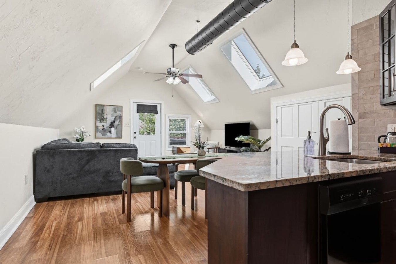 Une cuisine moderne dotée d’un îlot central, d’un coin repas avec des chaises, d’un ventilateur de plafond et de lucarnes.
