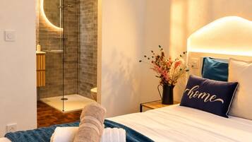 Una habitación de hotel con una cama, una mesita de noche, un florero con flores y una zona de ducha.