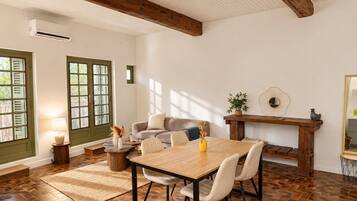 Un comedor con una mesa y sillas de madera, una mesita auxiliar con lámpara y vistas al exterior a través de una puerta con contraventanas.