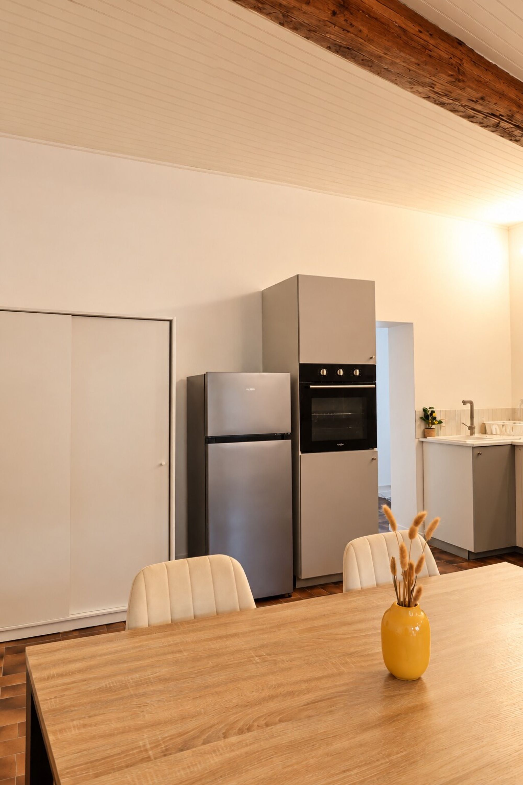 Una cocina moderna con horno integrado, refrigerador y un comedor con mesa y sillas de madera.