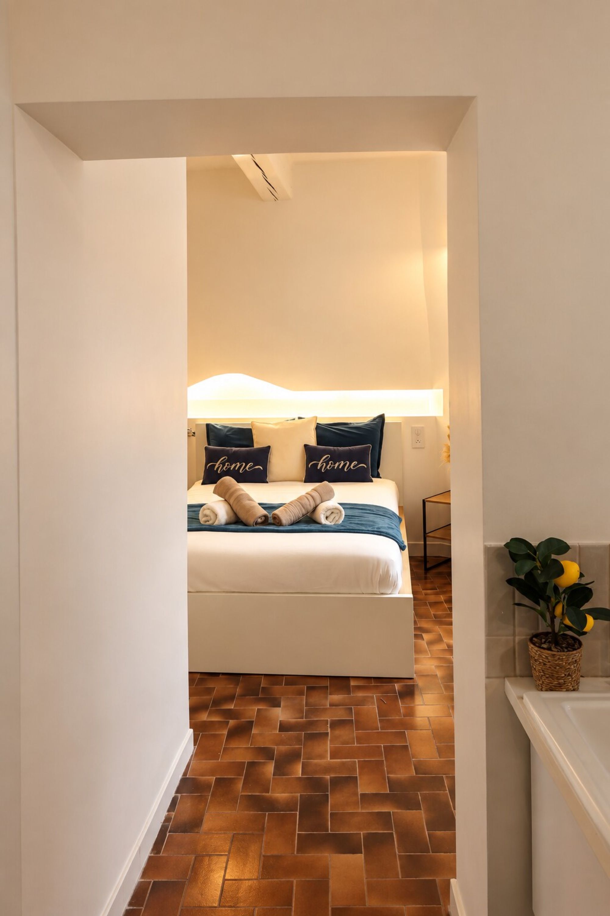 Une chambre d’hôtel avec un lit, une table de chevet, une lampe et une plante en pot.