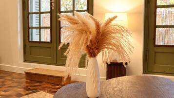 Una habitación con una mesa de madera, un florero blanco con plumas de pampa, una vela encendida y un control remoto.