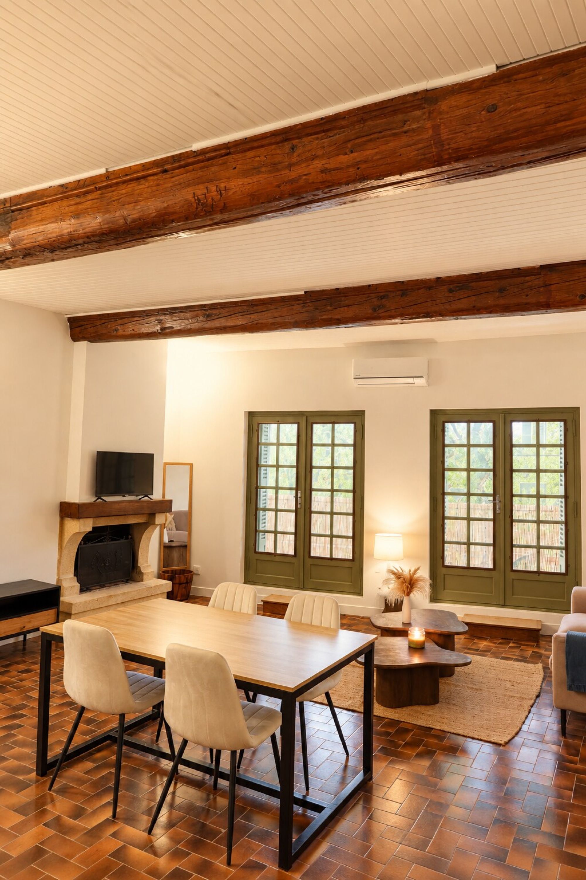 Una habitación amplia con techo de madera, chimenea, televisor y comedor con sillas y mesa.