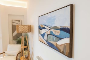 A room with a framed abstract painting on the wall, a wicker lamp, a globe on a wooden stand, and a white chair. - West Kirby Apartment Walk to Marine Lake & beach (West Kirby)