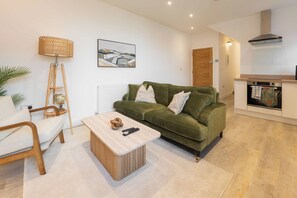 A modern living room with a green sofa, a wooden coffee table, a floor lamp, and a kitchen area with a stove and oven. - West Kirby Apartment Walk to Marine Lake & beach (West Kirby)