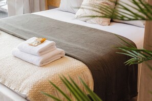 Un lit bien fait, avec une serviette pliée et une petite bouteille, une couverture grise à texture et un oreiller blanc.
