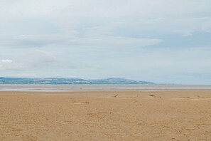 Une vaste plage de sable fin, avec une mer calme et des collines qui se dessinent à l’horizon.
