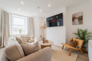 A modern living room with a sofa, a coffee table, and a TV mounted on the wall. - West Kirby Gem Walk to Marine Lake & beach (West Kirby)