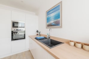 Eine moderne Küche mit weißen Schränken, einem eingebauten Ofen, einer Edelstahl-Spüle und einer Holzausziehtafel.