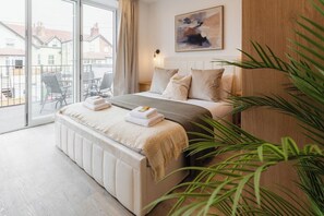 Ein Schlafzimmer mit großem Fenster, einem Bett mit weißem Kopfteil, einem Nachttisch und einer Pflanze.