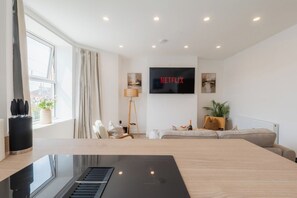 A modern living room with a large flat-screen TV, a piano, a sofa, and a coffee table. - West Kirby Gem Walk to Marine Lake & beach (West Kirby)