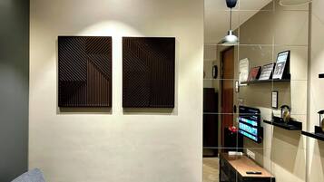 Een moderne woonkamer met een grijze bank, twee geometrische panelen aan de muur, een televisie op een standaard en een hanglamp.