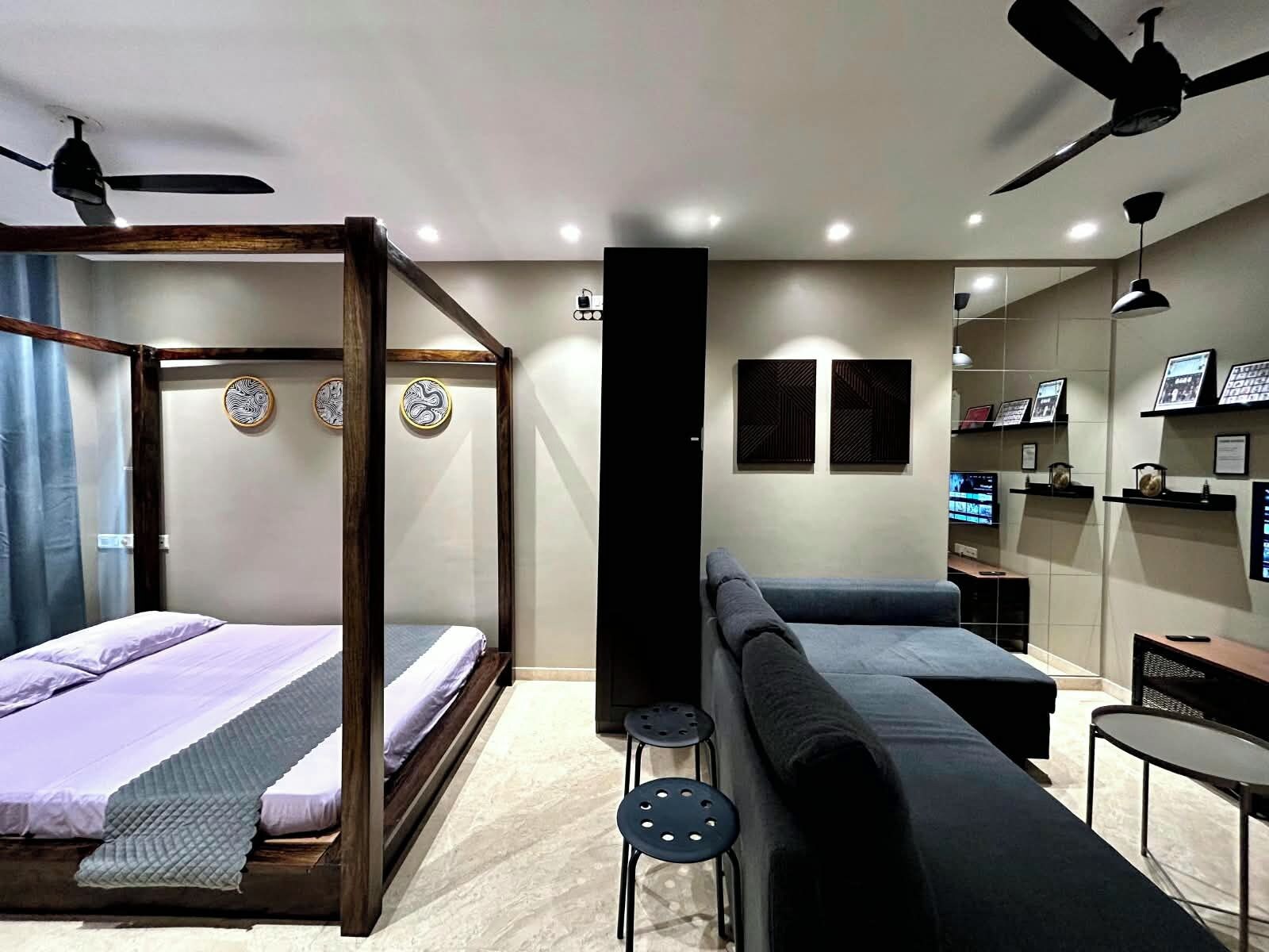 A modern bedroom with a four-poster bed, a sofa, a TV, and a ceiling fan.