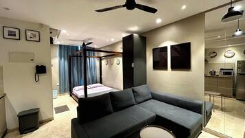 A modern bedroom with a large bed, a sofa, a small table, and a ceiling fan.