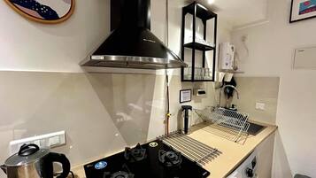A compact kitchen with a stove, a kettle, a built-in oven, and a microwave.