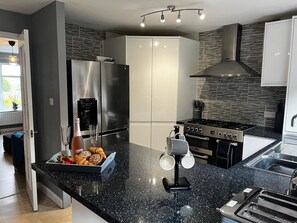 Une cuisine moderne dotée d’un plan de travail en granit noir, d’appareils électroménagers en acier inoxydable et d’un four encastré.