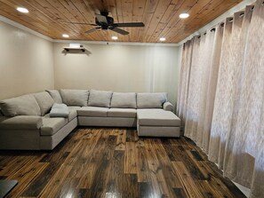A corner living room with a sectional sofa, wooden flooring, a ceiling fan, recessed lighting, and a window with curtains. - Spacious 4-bedroom house in Pioneer Ca with AC and Heat (Pioneer)