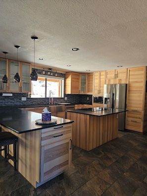 A modern kitchen with wooden cabinets, a stainless steel refrigerator, and a large island with a black countertop. - Spacious 4-bedroom house in Pioneer Ca with AC and Heat (Pioneer)
