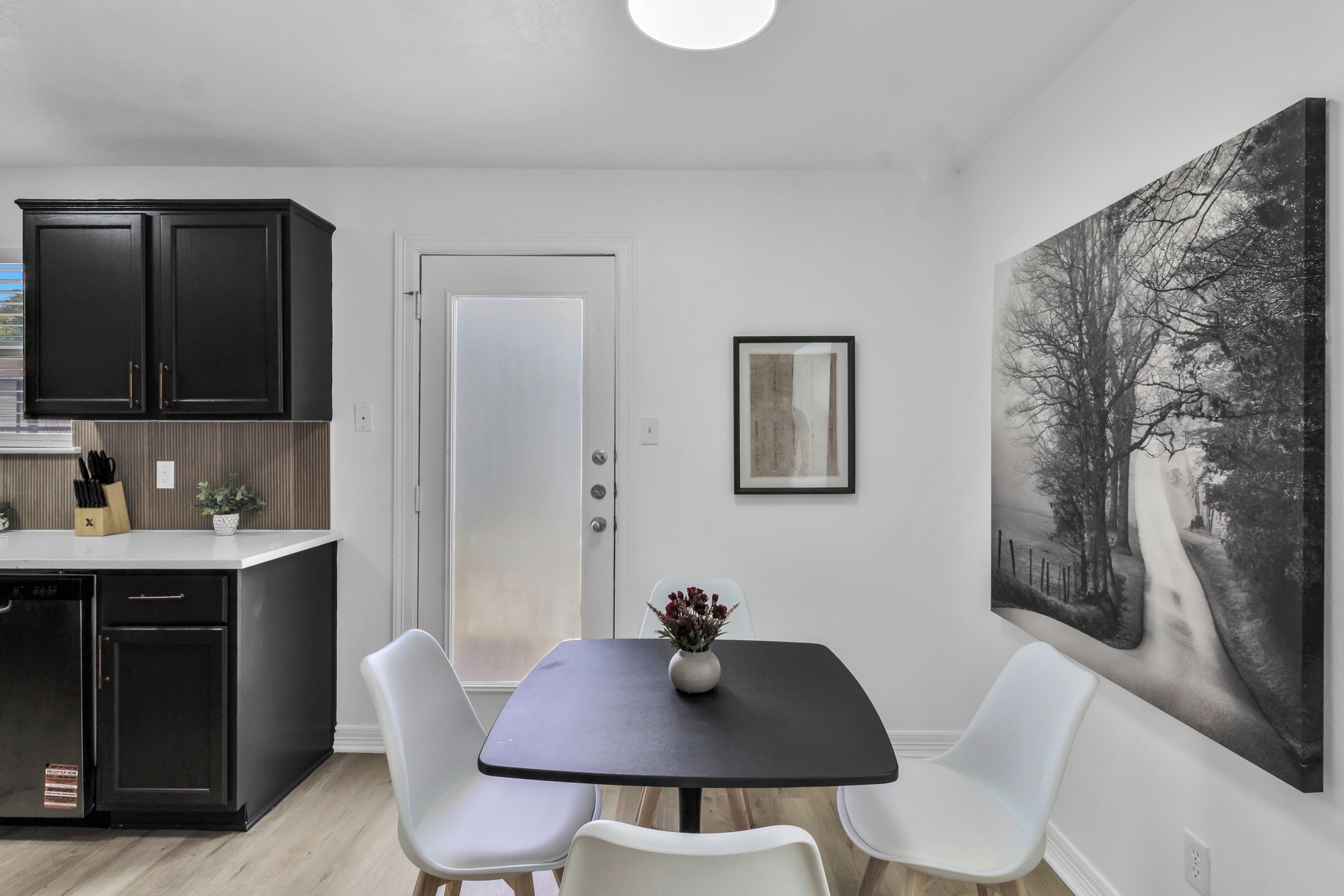 A modern kitchen with dark cabinets, a white door, and a dining area with a table and chairs.