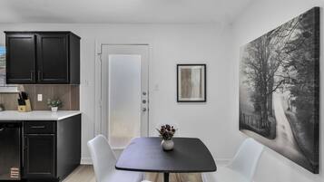 A modern kitchen with dark cabinets, a white door, and a dining area with a table and chairs.