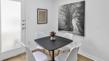 A dining area with a table and four chairs, a vase with flowers, and two artworks on the wall.