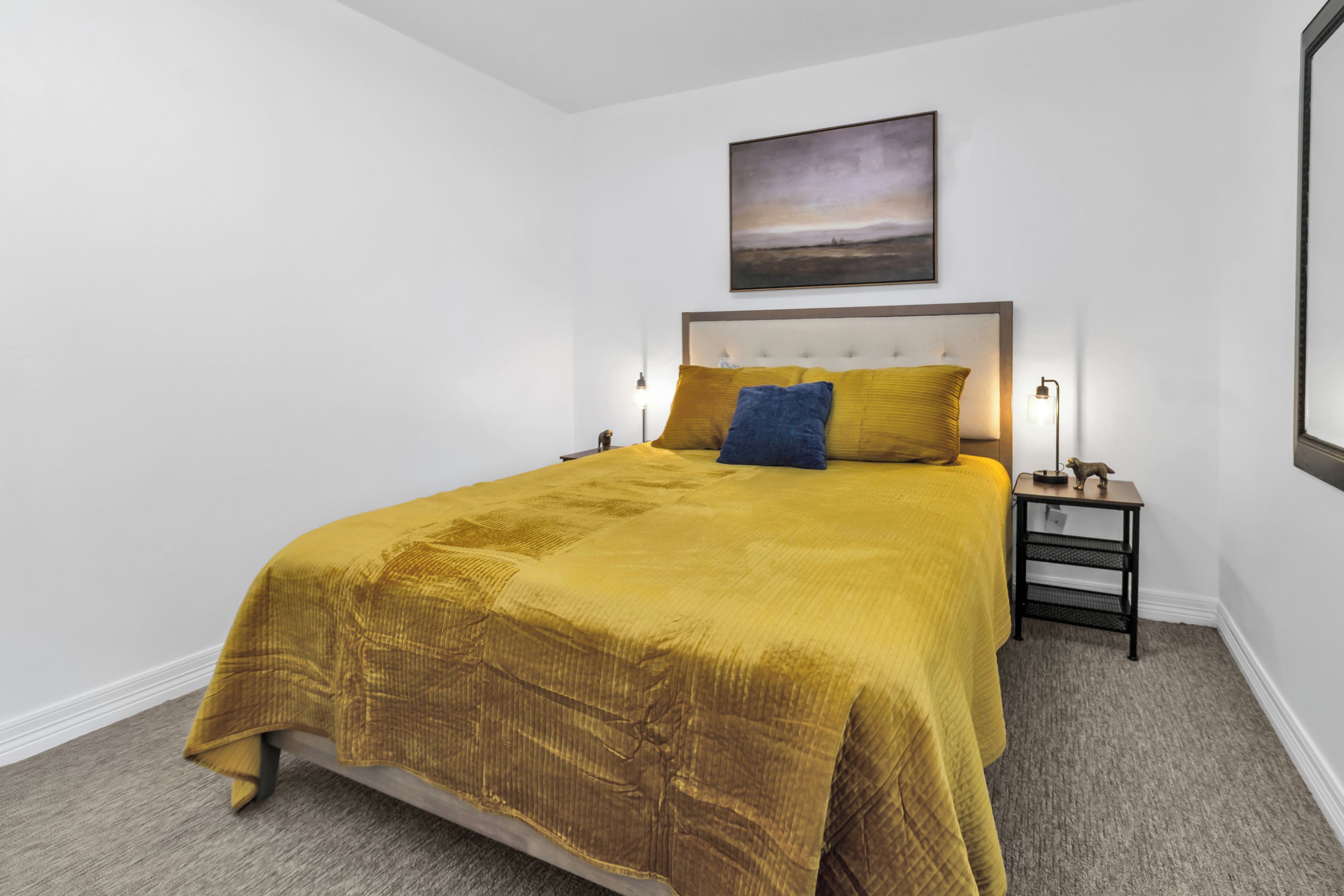 Een hotelkamer met een groot bed, een nachtkastje, een lamp en een schilderij aan de muur.